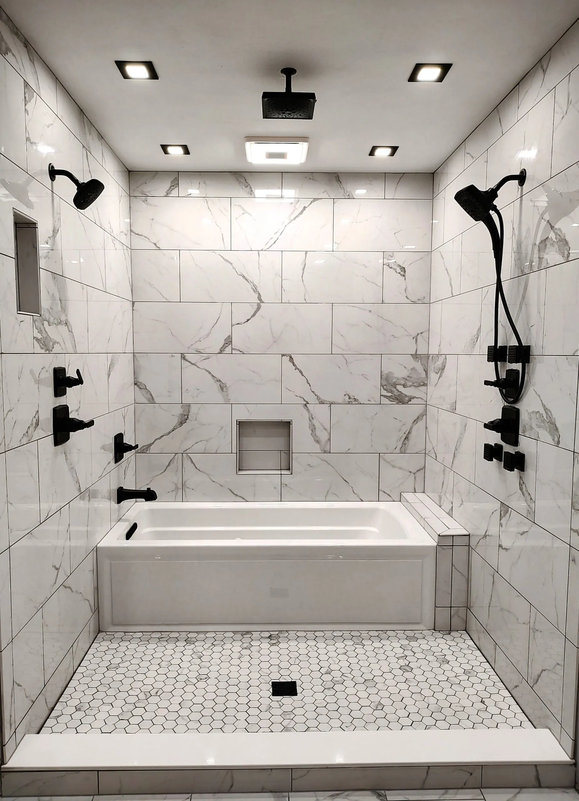 Marble tiled tub surround with black shower fixtures and a hexagon tile floor