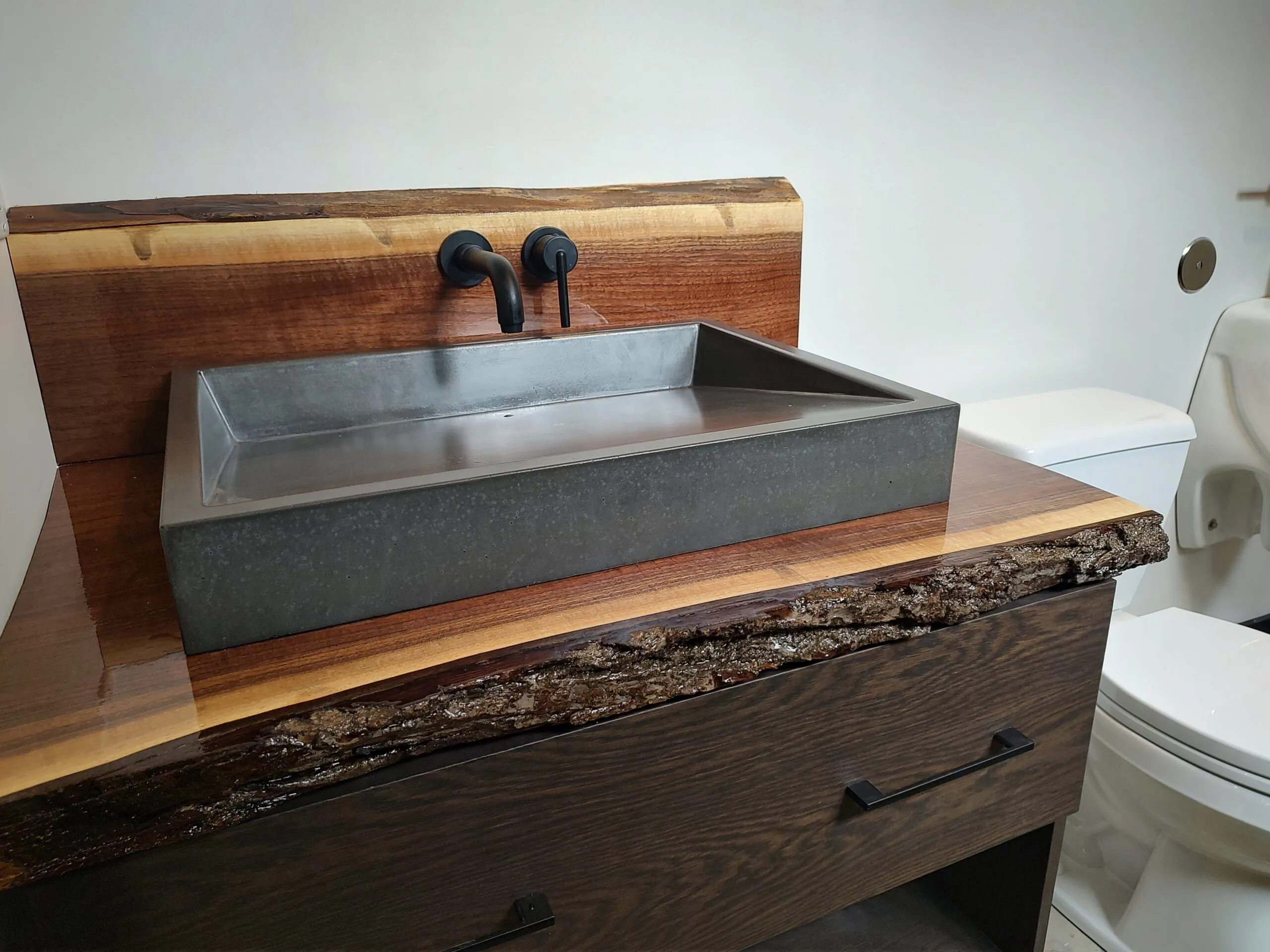 Concrete trough sink on a live edge walnut vanity with a black wall mount faucet