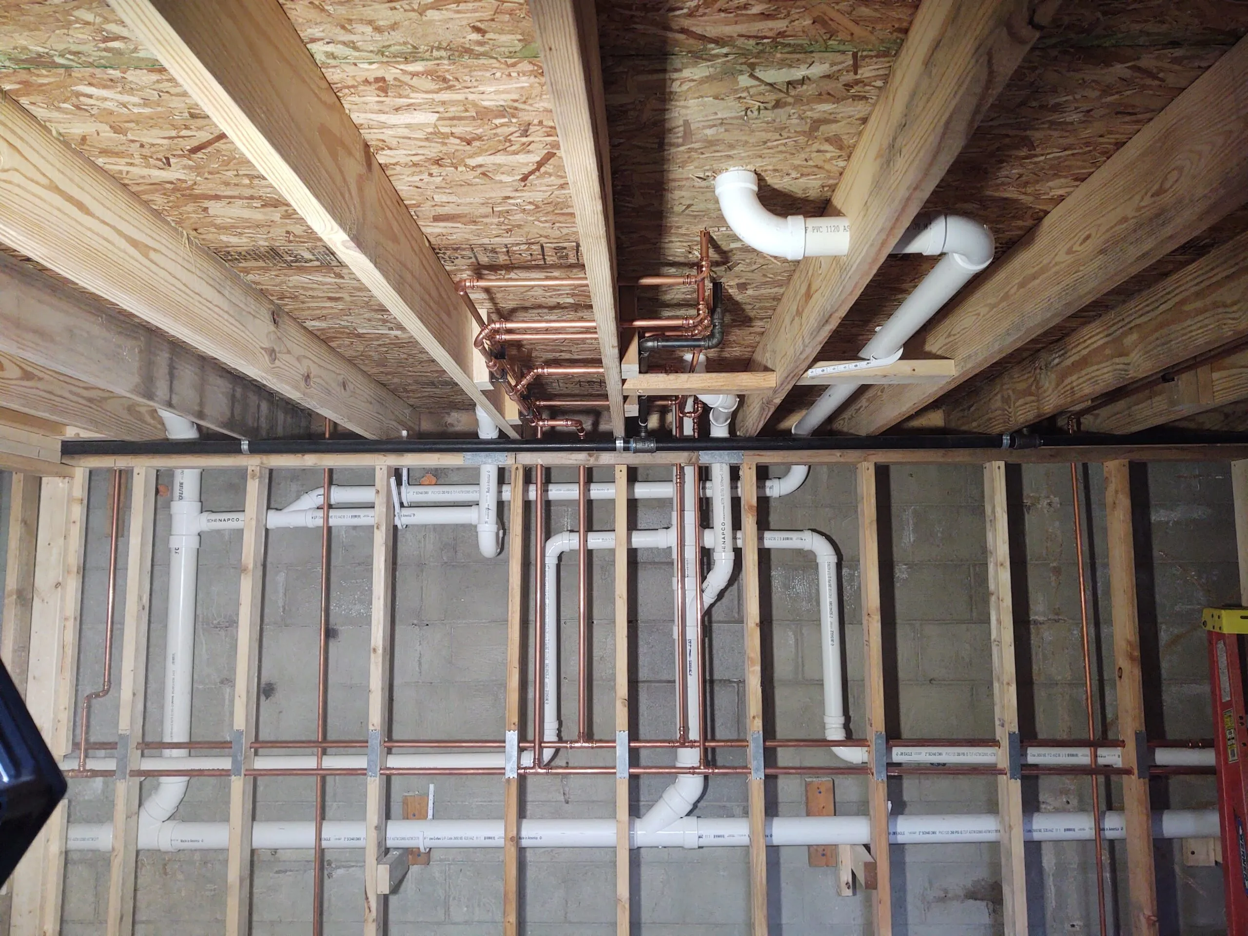 Copper water lines and PVC waste piping roughed in through basement floor joists